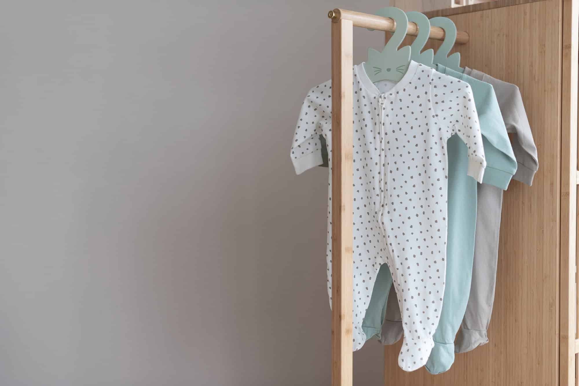 Three baby boy onesies, one white with polka dots, hanging on cute cat-shaped hangers on a wooden rack.