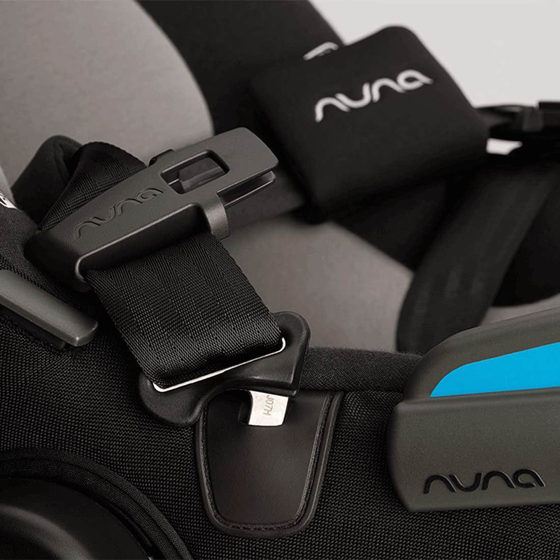 Close-up of a Nuna car seat with black fabric, harness, buckle, and chest clip details.