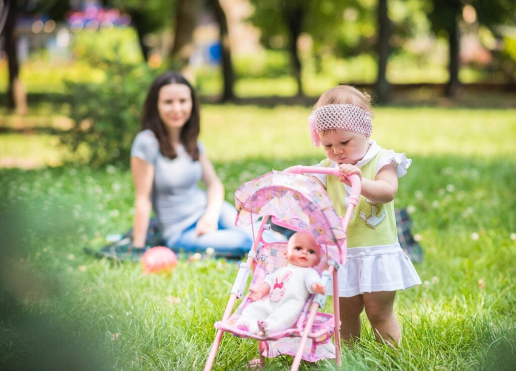Best baby doll with stroller set being walked by a toddler on the grass on a sunny day